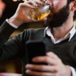 Man holding mobile phone and having a drink in bar