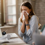 Young sick businesswoman sneezing in a tissue while working in the office.