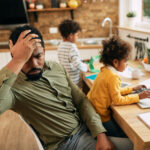 African American stay at home father feeling displeased while babysitting his kids and working at home.